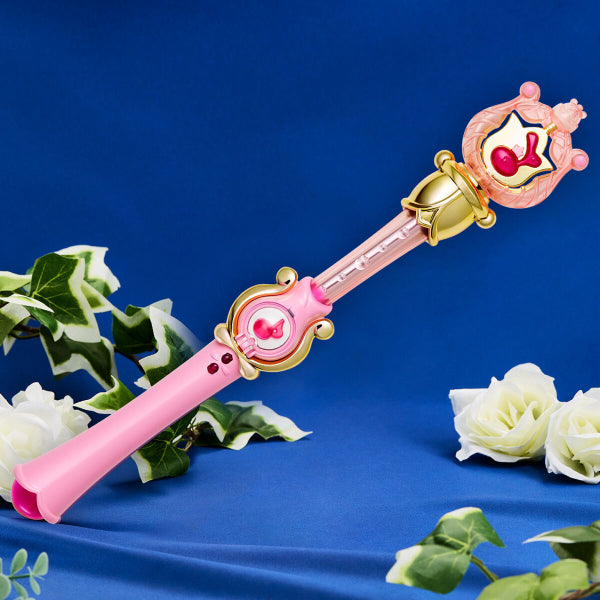 A pink and gold magical wand with character motifs from the anime Ojamajo DoReMi, displayed on a blue background with white flowers.