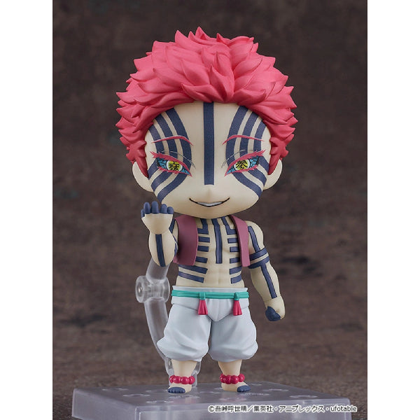 A Nendoroid action figure of Akaza from the anime series 'Demon Slayer', with a smiling face, wearing a white and pink outfit, holding a staff, and displaying a serious expression.